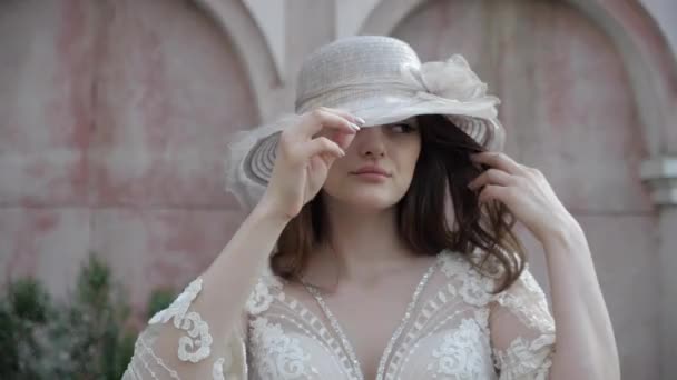 Bonita morena con largo pelo rizado suelto sostiene sombrero blanco — Vídeos de Stock