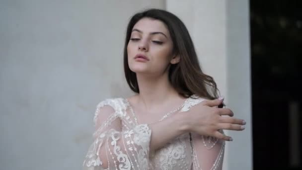 Lady in white lacy dress with bell sleeves fixes long hair — Stock Video