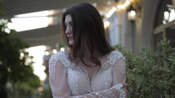 Молодая женщина в свадебном платье фиксирует волосы стоя на улице — стоковое видео