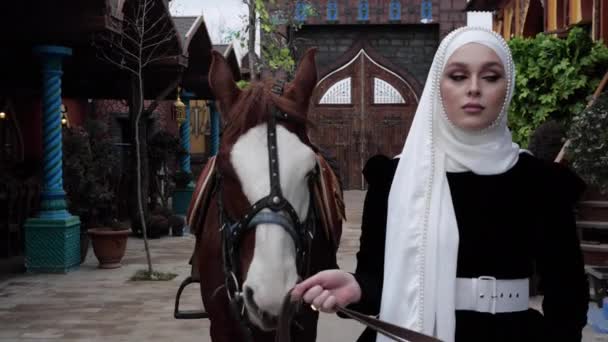 Chica en tradicional blanco shayla conduce caballo a lo largo de patio — Vídeos de Stock