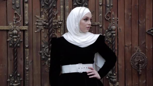 Chica en vestido oriental posa cerca de puertas de madera con detalles — Vídeos de Stock