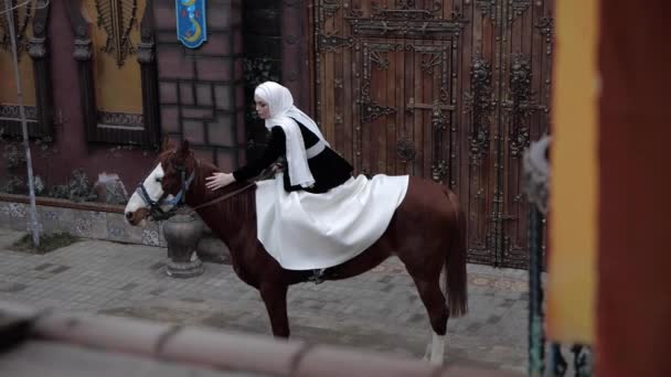 Mujer árabe en shayla golpes caballo castaño cerca de la puerta — Vídeos de Stock