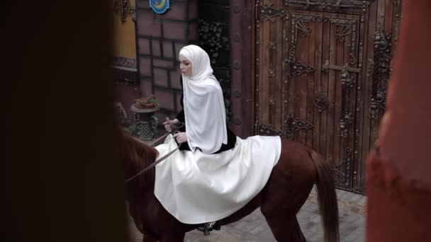 Femme en costume arabe monte cheval châtain près de la porte en bois — Video