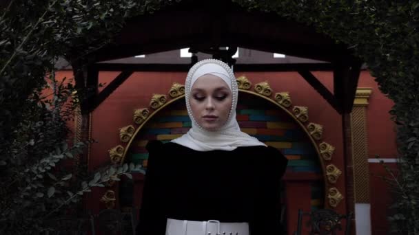 Жінка з білим поясом і пози хіджабу біля зеленої арки — стокове відео