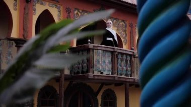 Shayla 'lı kız teras manzaralı sütun arkasından duruyor.