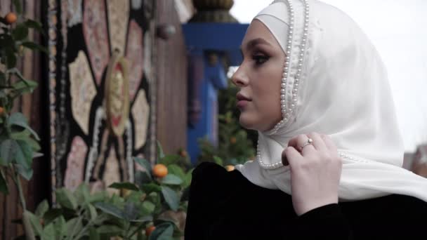 Woman in traditional Arabian clothes adjusts white hijab — Stock Video