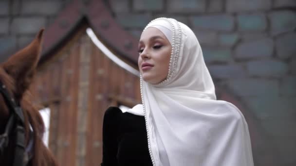 Девушка в арабском костюме и хиджабе с жемчугом сидит на лошади — стоковое видео