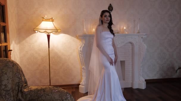 Молодая женщина в длинном обтягивающем платье стоит у камина — стоковое видео