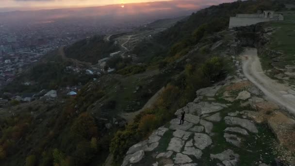 Joven mujer de pie en el borde del cañón de Tarki y observa la ciudad — Vídeos de Stock