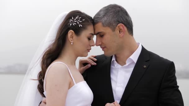 Романтические свадебные объятия, стоящие против серой реки — стоковое видео