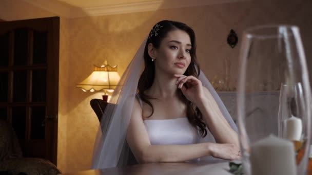 Sad brunette in white wedding dress sits at table and cries — Stock Video