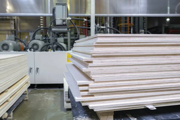 Stacked plywood and wooden board products against de-focused blurred piece of industrial warehouse storage on production site. Copy space. Selective focus. — ストック写真