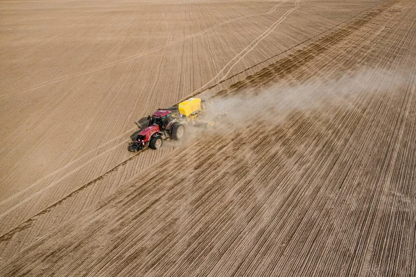 Aerial view of tractor with mounted seeder performing direct seeding of crops on plowed agricultural field. Farmer is using farming machinery for planting process, top view