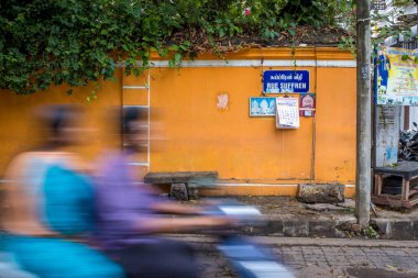Pondicherry, Hindistan - 17 Mart 2018: Turuncu bir duvarın önünden geçen tanınmayan bir çift ve hareket bulanıklığı olan bir scooter ile sokak tabelası