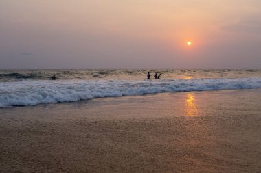 Varkala, Kerala, Hindistan - 1 Nisan 2018: Günbatımında Varkala sahilinde yüzücüler. Güneşli bir bahar öğleden sonra çekildi..