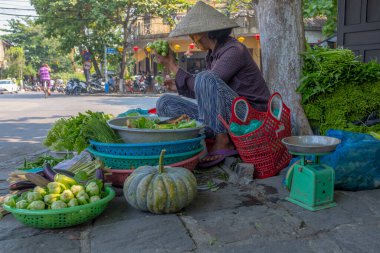 Hoi An, Vietnam - 12 Nisan 2018: Sokakta sebze satan ve kameraya bakmayan bir kadın