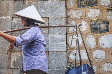 Hanoi, Vietnam - 1 Mayıs 2018: Boyunduruk sepetleri taşıyan, geleneksel başıboş şapka takan, arka planında taş duvar olan kadın