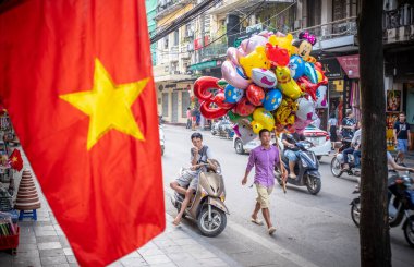 Hanoi, Vietnam - 30 Nisan 2018: Yerel satıcının ön planda bir demet renkli balon ve Vietnam bayrağı taşıdığı sokak sahnesi