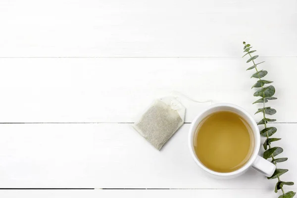 Morning tea cup with Eucalyptus Silver Dollar plant leaves on white wood panel background