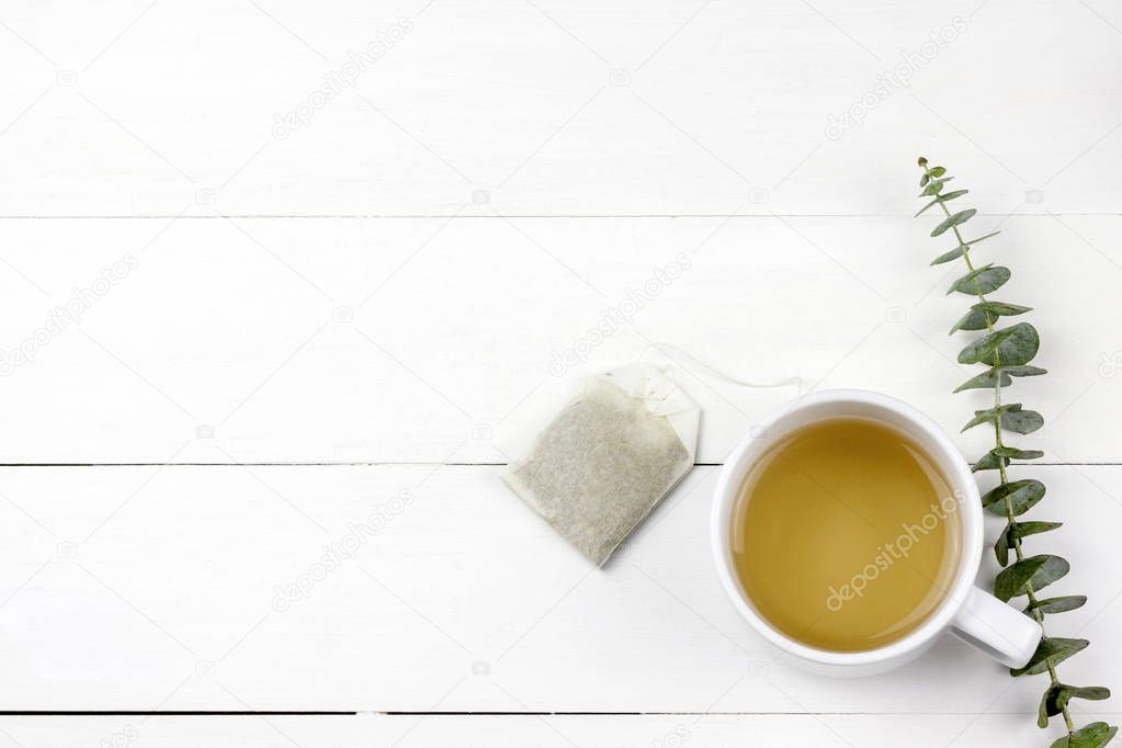 Morning tea cup with Eucalyptus Silver Dollar plant leaves on white wood panel background