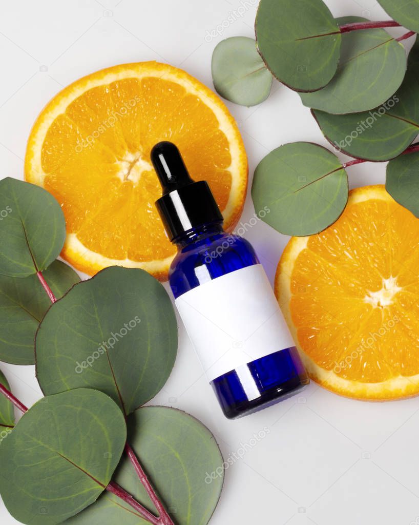 Blue glass skin care bottle decorate with fresh half oranges and leaves on white background photo