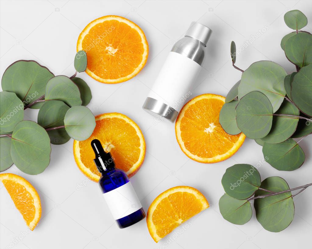 Blue glass and silver metal skin care bottle decorate with fresh half oranges and leaves on white background photo