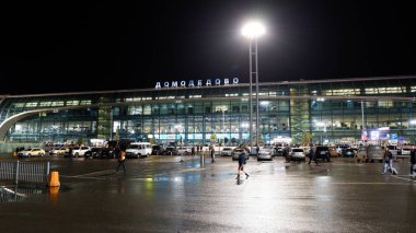 Moskova / Rusya - 18 Ekim 2019: Gece vakti uluslararası Domodedovo havaalanı binasının dışı. İnsanlar terminalin yanında yürüyorlar. Parlak ışıklar parlıyor.