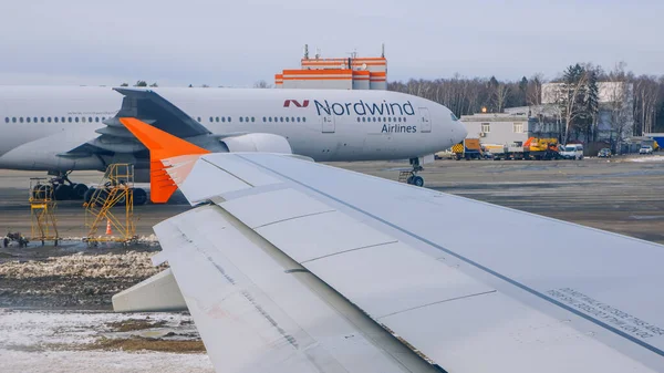 Sheremetyevo Havaalanı 'ndaki uçak penceresinden kanat manzarası. Arka planda - Boeing 777 Nordwind Havayolları ve Sheremetyevo Havaalanı 'ndaki farklı vihicles