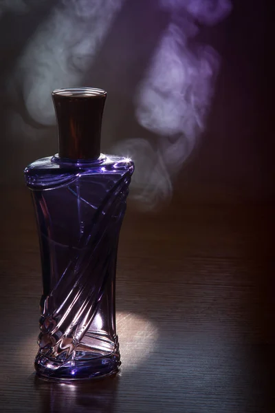 Hermosa botella púrpura perfume femenino en el humo — Foto de Stock