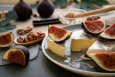 Dengeli beslenme için bileşim. Gri bir masada ballı ve dilimlenmiş incirli peynirli camembert peyniri ve bulanık arka planda yeşil yaprakların arka planı..