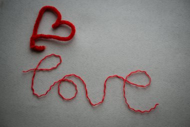 Aşk kelimesi kırmızı ipliklerle yazılır ve gri bir çantada duyulur.
