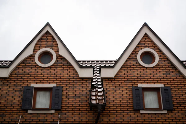 Yuvarlak pencereli kırmızı tuğlalı binanın çatıları. Açık gri sonbahar yağmurlu gökyüzünün arka planında.