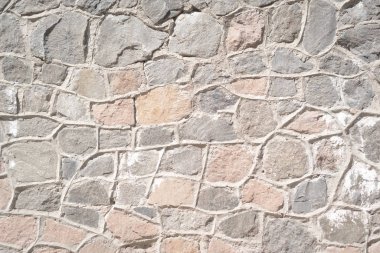 Taştan bir duvar güneş tarafından aydınlatılır. Farklı boyutlarda taşlarla arka planda yerleşin.