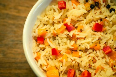 Zerdeçal ya da safran sebzeli pilav. Tahta yüzeyde beyaz kasede kırmızı dolma biberli vejetaryen yemeği..