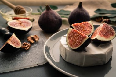 İncir, bal ve cevizli peynirli peynir gri bir tabakta servis ediliyor ve arka planda taze yapraklar var. Dengeli beslenme için inek sütü proteiniyle tatlı meyve dilimleyin.