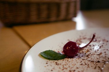 Nane yapraklı kırmızı vişne kokteyli tabağı süslüyor. 