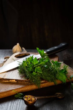 Maydanoz ve dereotu, mutfakta ahşap bir yüzey üzerinde sağlıklı yemek pişirmek için. Etrafta biberli bir bıçak ve metal kaşık var..