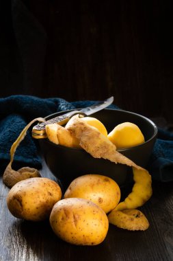 Masadaki kasede soyulmamış bir avuç çiğ sebzeyle birlikte bıçak ve soyulmuş patates. Evde yemek var..