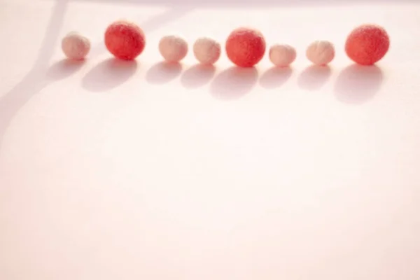 Wool balls are thrown down by the sloping needle method, scattered at the top of the postcard on a smooth pink background.