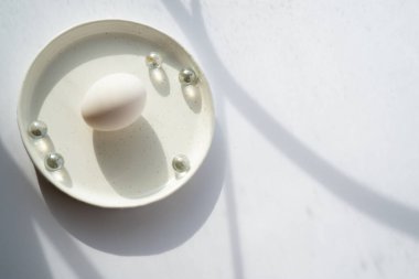 Parlak bahar güneşini yansıtan küçük cam toplarla beyaz bir tabakta tavuk yumurtasıyla kompozisyon.