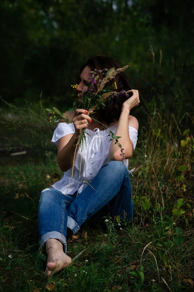 Женщина Джинсах Белой Блузке Открытыми Плечами Сидит Свежей Траве Букетом — стоковое фото