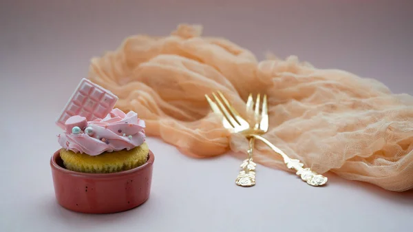 Pembe bir yüzey üzerinde açık sarı bir havlu üzerinde klasik altın çatallar. Yanında da kremalı lezzetli kekler..