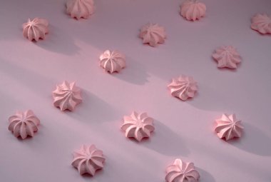 Girl's air bisexual or meringue on a delicate pink background. Baked sweet dessert made of beaten eggs is laid out in equal rows on a light surface.