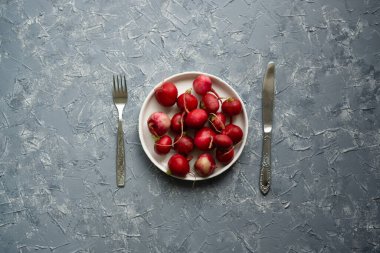 Masanın ortasında çatal ve bıçakla gri yüzeyde beyaz tabakta olgun turp..