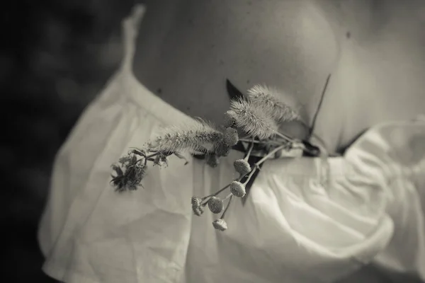 Beyaz bluzlu çekici bir kadının çıplak omzunda yakasında duran narin kır çiçekleri demeti. Sevdiğin biriyle aşk ve barış.