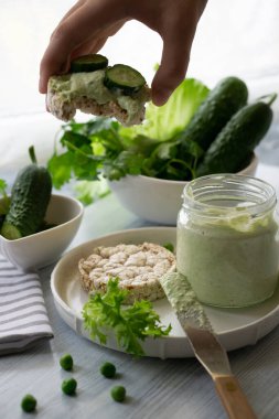 Yeşil krem peynirli kuru ekmekli ekşi tost ve çocuğun elindeki salatalık dilimleri bahar vitaminleriyle dolu bir tabakta.
