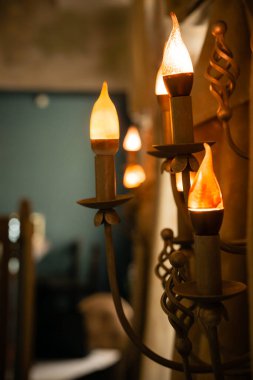 Bir avizenin içinde mum şeklinde bir duvar lambası ve sıcak bir odanın ışıkları..
