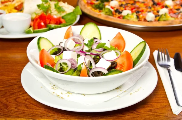 Frisk grekisk sallad i en skål med andra rätter i bakgrunden — Stockfoto