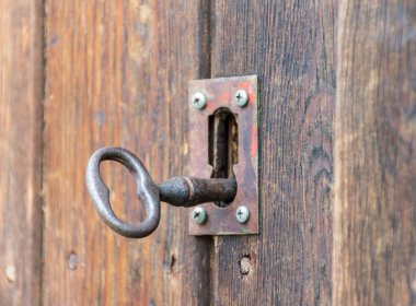 Eski ya da eski bir anahtar. Ahşap bir kapının kilidi içindeki metalik demirden yapılmış. Eski anahtar ve kilit tamamen paslanmış ve kapıyı açmaya hazır. Kimseyle yatay fotoğraf.