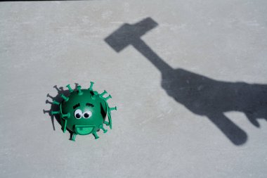 Conceptual photo of a shadow of a hand holding a hammer. The hammer shadow looks to beat a toy green virus looking to other side, unprepared, on a grey background. clipart